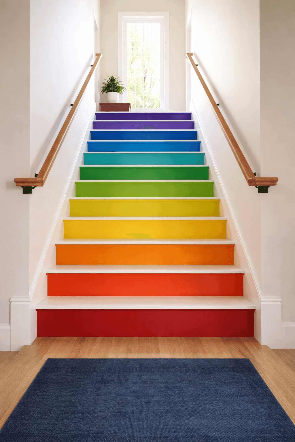 Bold rainbow painted staircase with vibrant colored risers from red to purple creating dramatic gradient effect in modern home