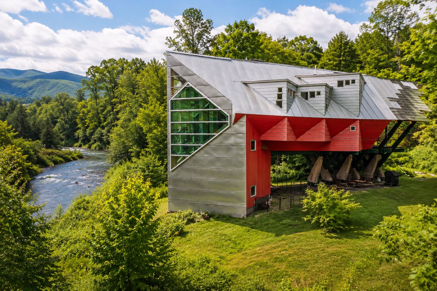 A striking angular red and silver home elevated on stilts over a lush Vermont riverbank, designed by Yestermorrow founder John Connell